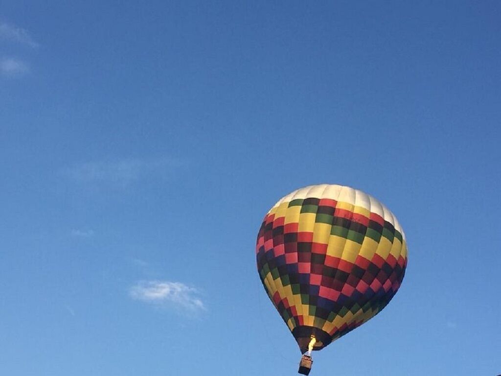 Een luchtballon met een kleurrijk geruit patroon tegen een helderblauwe lucht.