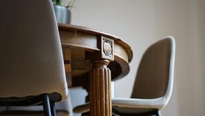 Una mesa redonda de madera con pata labrada, rodeada por dos sillas con patas de metal negro.