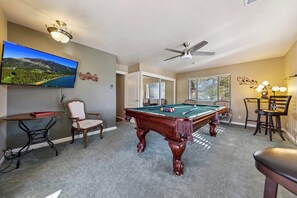 Ein Billardtisch in einem Raum mit Deckenventilator, Fernseher und einem Fenster mit Jalousien.