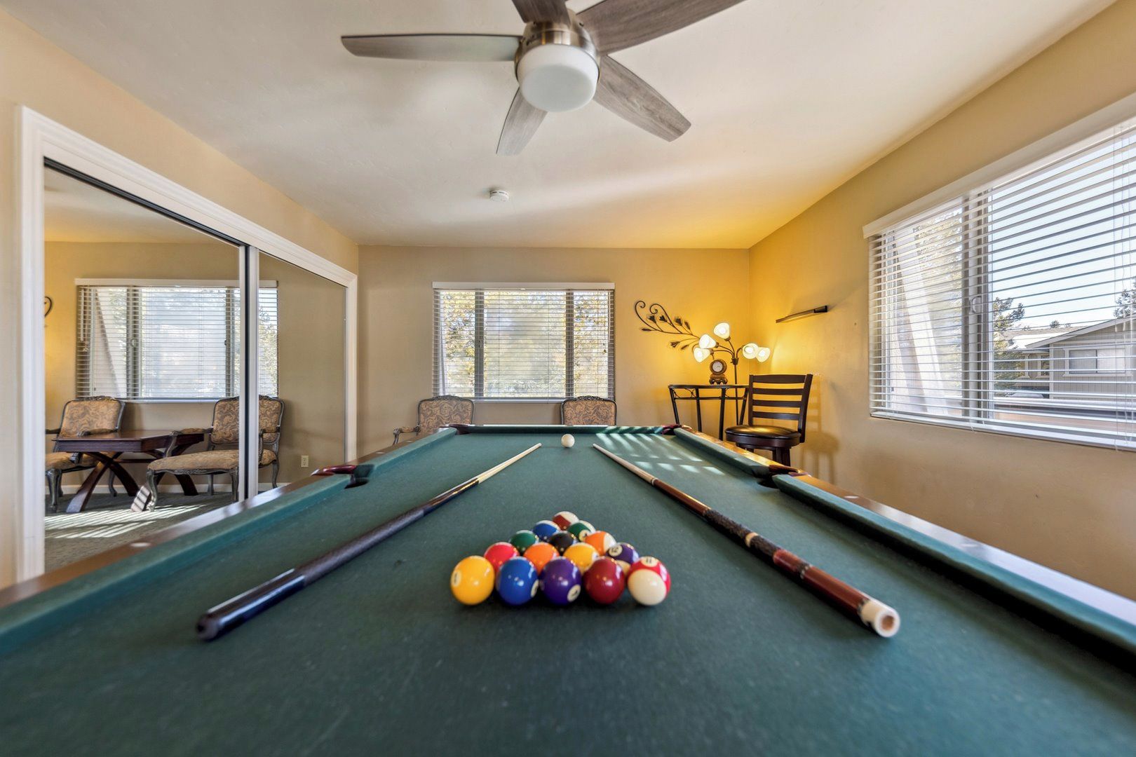 A pool table with balls, a ceiling fan, and a window with blinds.