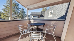 A covered balcony with a round table and four chairs, overlooking a residential area with houses and trees. - Spacious Tahoe Retreat with Rooftop Deck & Mountain Views (South Lake Tahoe)