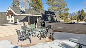 A covered outdoor patio with a glass table and chairs, surrounded by snow. - Spacious Tahoe Retreat with Rooftop Deck & Mountain Views (South Lake Tahoe)