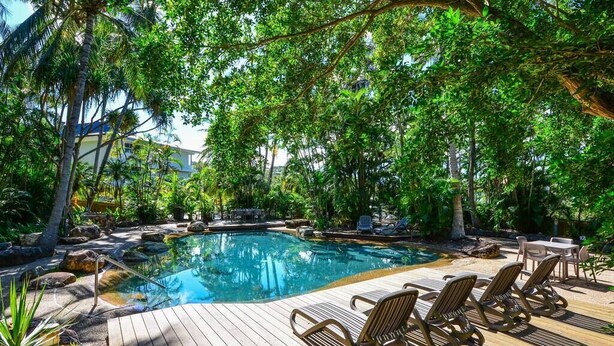 A wooden deck with lounge chairs and a swimming pool surrounded by lush greenery. - Poinciana Lodge 103 (Hamilton Island)