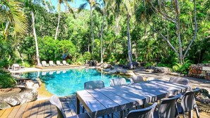A pool area with lounge chairs and a table, surrounded by tropical vegetation. - Poinciana Lodge 103 (Hamilton Island)