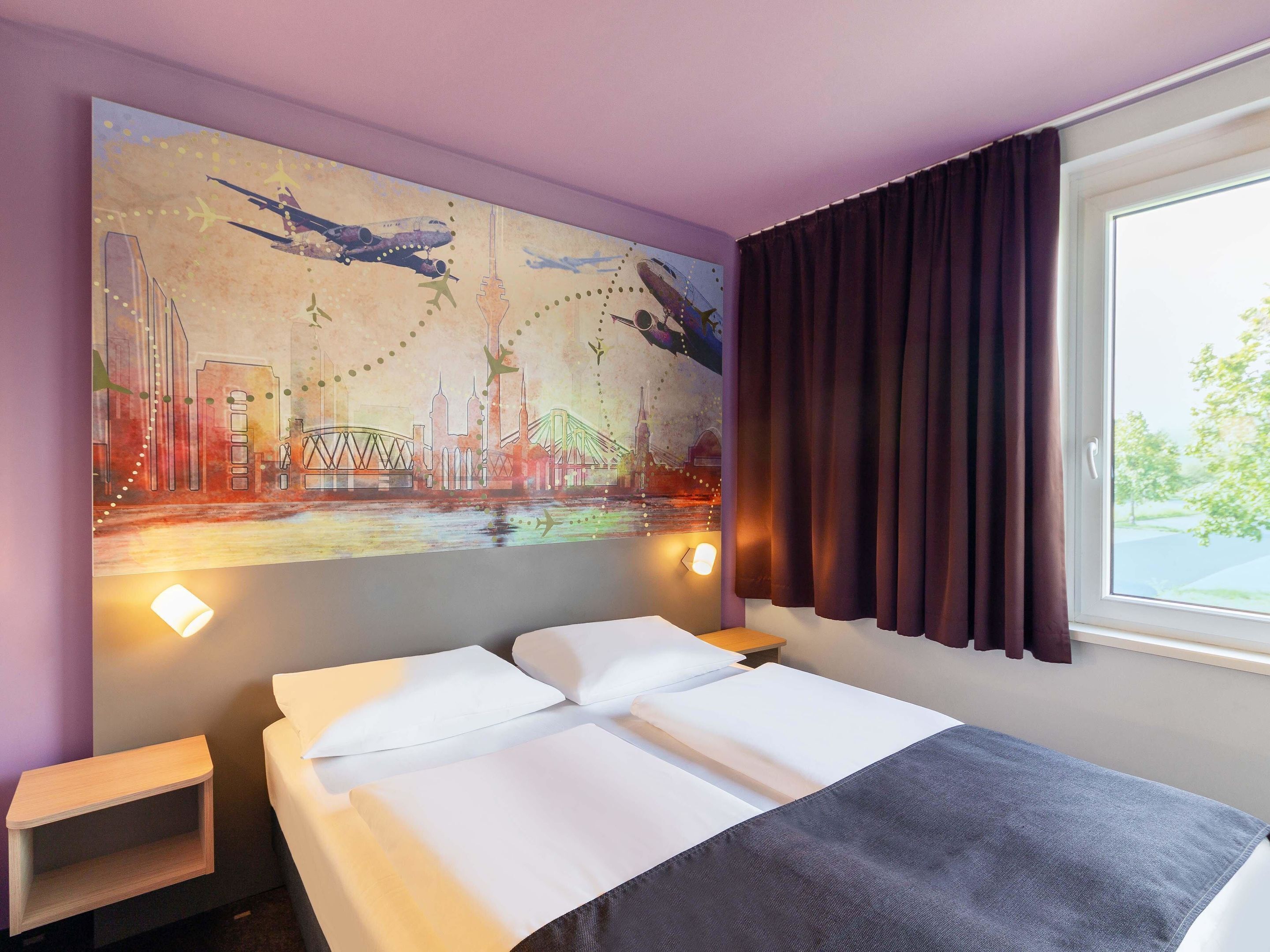 A hotel room with a bed, a nightstand, a wall-mounted lamp, and a window with curtains.