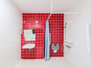 Un baño con pared de baldosas rojas, un lavamanos blanco, un espejo, una ducha con cortina azul y un inodoro blanco.