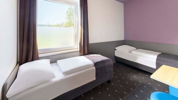 A hotel room with two beds, a small table, and a view of the outdoors. - B&B Hotel Düsseldorf-Airport (Düsseldorf)