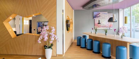 A modern reception area with a wooden reception desk, blue stools, and potted orchids.