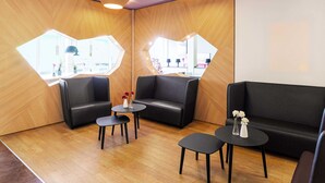 A modern waiting area with black leather seating, wooden accents, and a large window providing a view of the interior. - B&B Hotel Düsseldorf-Airport (Düsseldorf)
