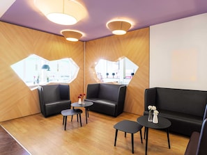 A modern waiting area with black leather seating, wooden accents, and a large window providing a view of the interior. - B&B Hotel Düsseldorf-Airport (Düsseldorf)