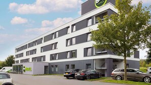 A modern B&B hotel with a flat facade, multiple windows, and a parking area with cars.