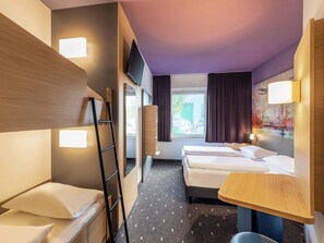 Habitación de hotel con literas, un escritorio, una silla, un televisor y una ventana con cortinas.