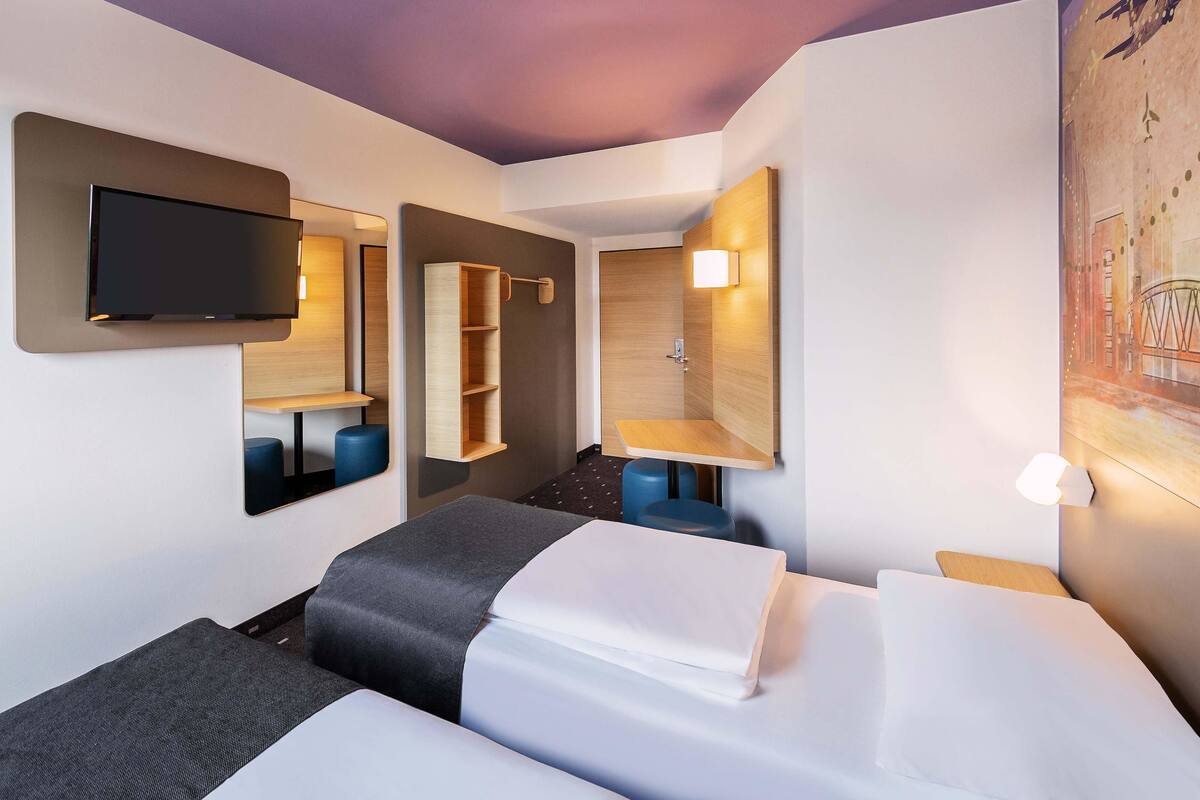 Una habitación de hotel con una cama, un televisor, un estante de madera y un cuadro en la pared.