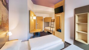 A modern hotel room with a bunk bed, a desk, a chair, a mirror, and a television.