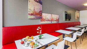 A modern restaurant with red booths, white tables, and artwork on the walls.