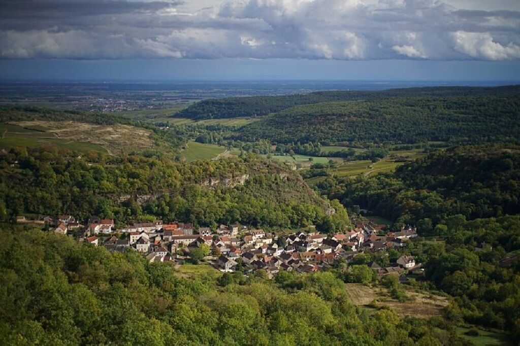 Ein Dorf eingebettet in ein Tal, umgeben von grünen Hügeln und Häusern.