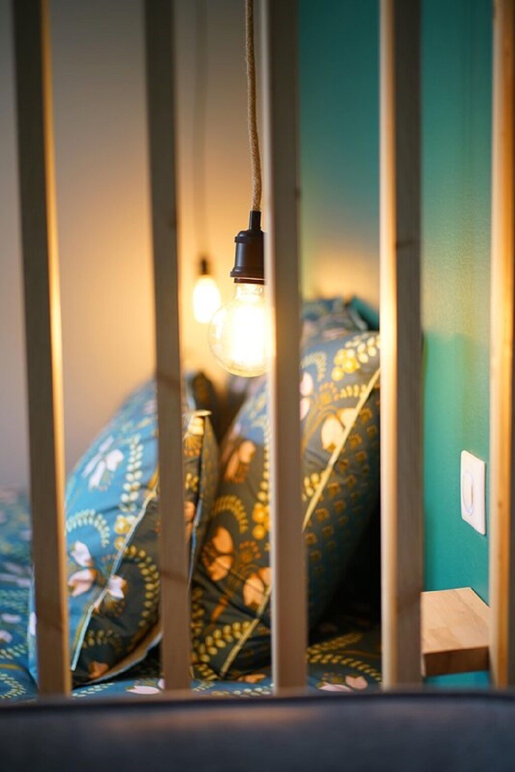 Une pièce avec un lit recouvert d’une literie à motifs, une ampoule suspendue et une prise électrique au mur.