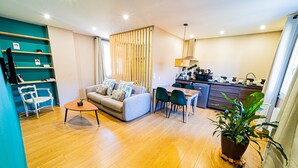Una sala de estar moderna con sofá, una mesa de comedor y sillas, una zona de cocina con microondas y fregadero, y piso de madera.