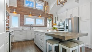 Une cuisine moderne avec des meubles blancs, un mur d’accent en bois, un grand îlot central doté de tabourets et des appareils électroménagers en acier inoxydable.