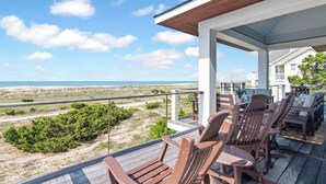 Une terrasse en bois, agréée de mobilier d’extérieur, qui offre une vue sur une plage et l’océan.