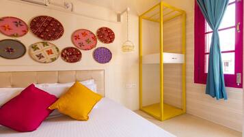 A bedroom with a bed, colorful wall decorations, a yellow wardrobe, and a window with curtains.