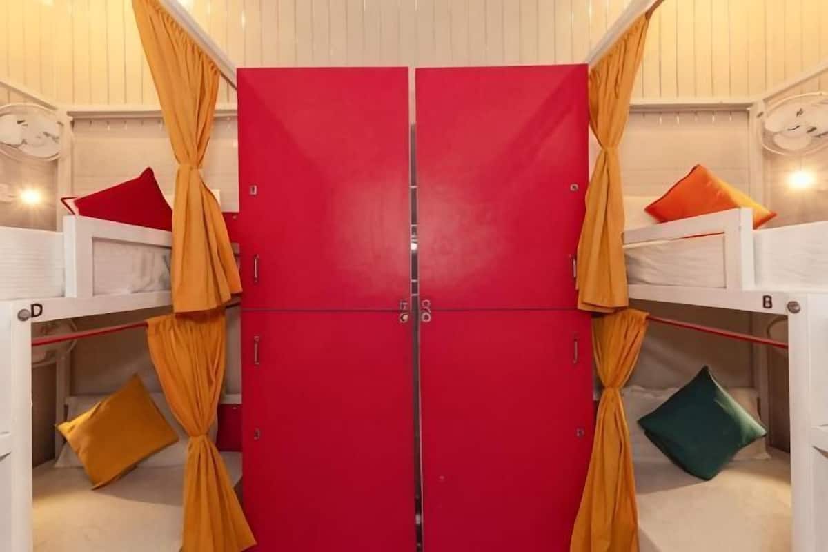 A room with a red wardrobe, two beds with pillows, and a window.