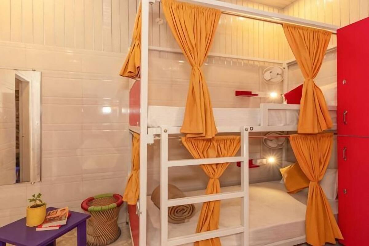 A bunk bed with curtains, a small table with a plant, a trash bin, and a red cabinet.