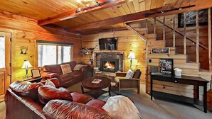 Ein gemütliches Blockhaus-Interieur mit Kamin, Ledersofas und einer Holztreppe.