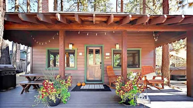 Eine Holzjagdhaus mit Veranda, Grill und Sitzgelegenheit im Freien.