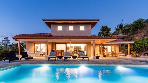 Una casa moderna con piscina, mobiliario exterior y un patio cubierto.
