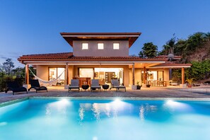 Ein modernes Haus mit Pool, Sitzgelegenheiten im Freien und einer überdachten Terrasse.