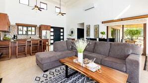 Amplia sala de estar con un sofá gris, una mesa de centro de madera y una cocina al fondo.
