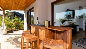 Una zona de bar con barra de madera, taburetes, una botella de vino y vasos.