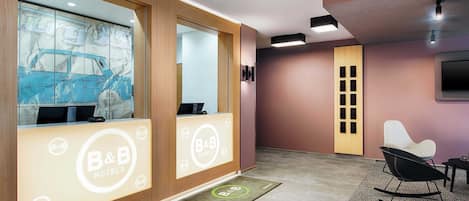 Uma área de recepção de hotel com design moderno, incluindo um balcão de atendimento, uma grande janela com desenho de um carro e uma área de estar com uma cadeira de balanço.