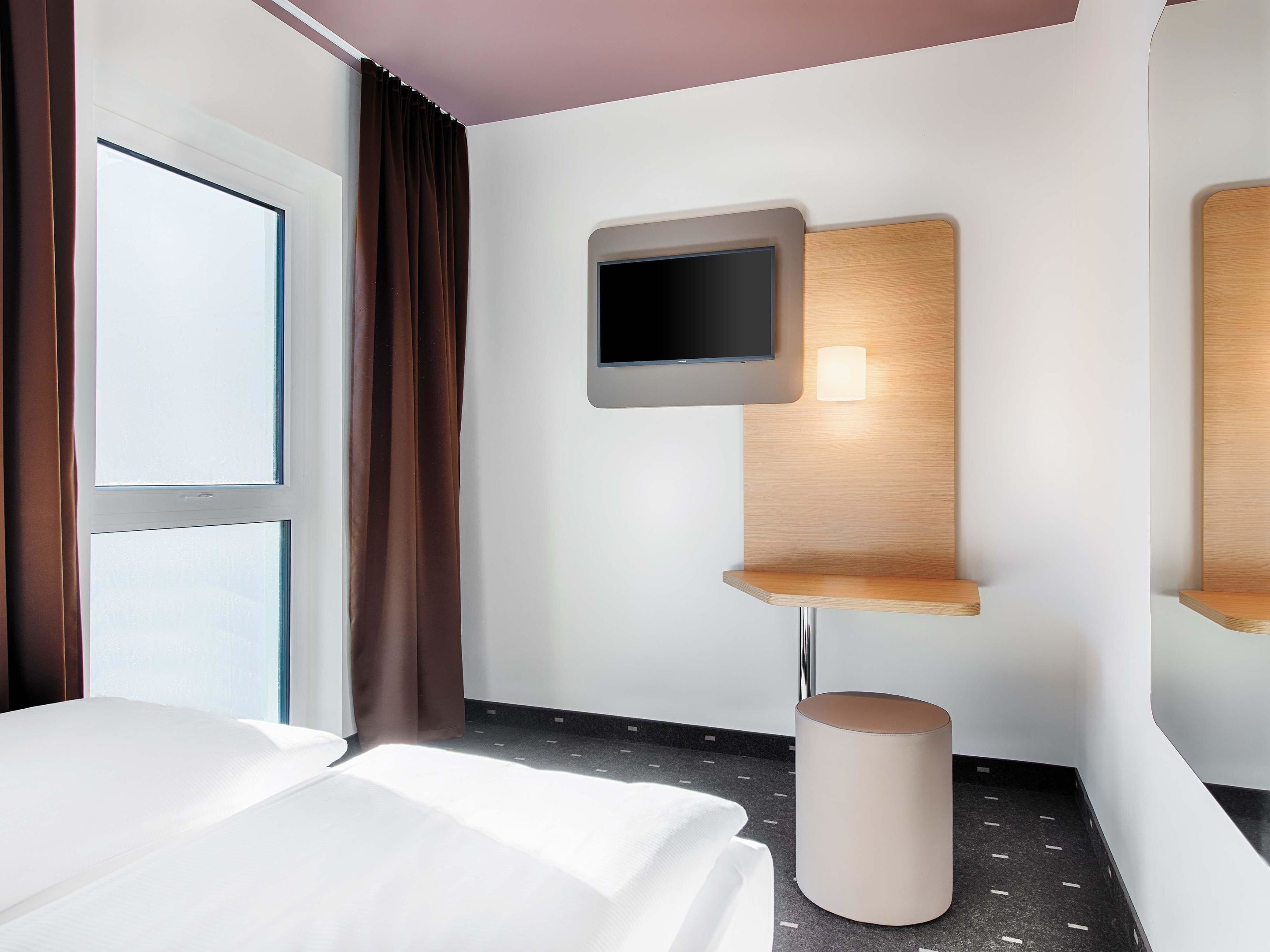 Ein Hotelzimmer mit Bett, Fernseher an einer Holzwand, einem kleinen Tisch und einem Mülleimer.