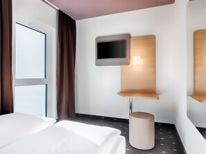 A hotel room with a bed, a television mounted on a wooden panel, a small table, and a trash bin. - B&B Hotel Eisenach (Eisenach)
