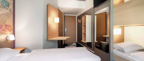 A modern hotel room with a large bed, a bedside table, a mirror, and built-in shelving.
