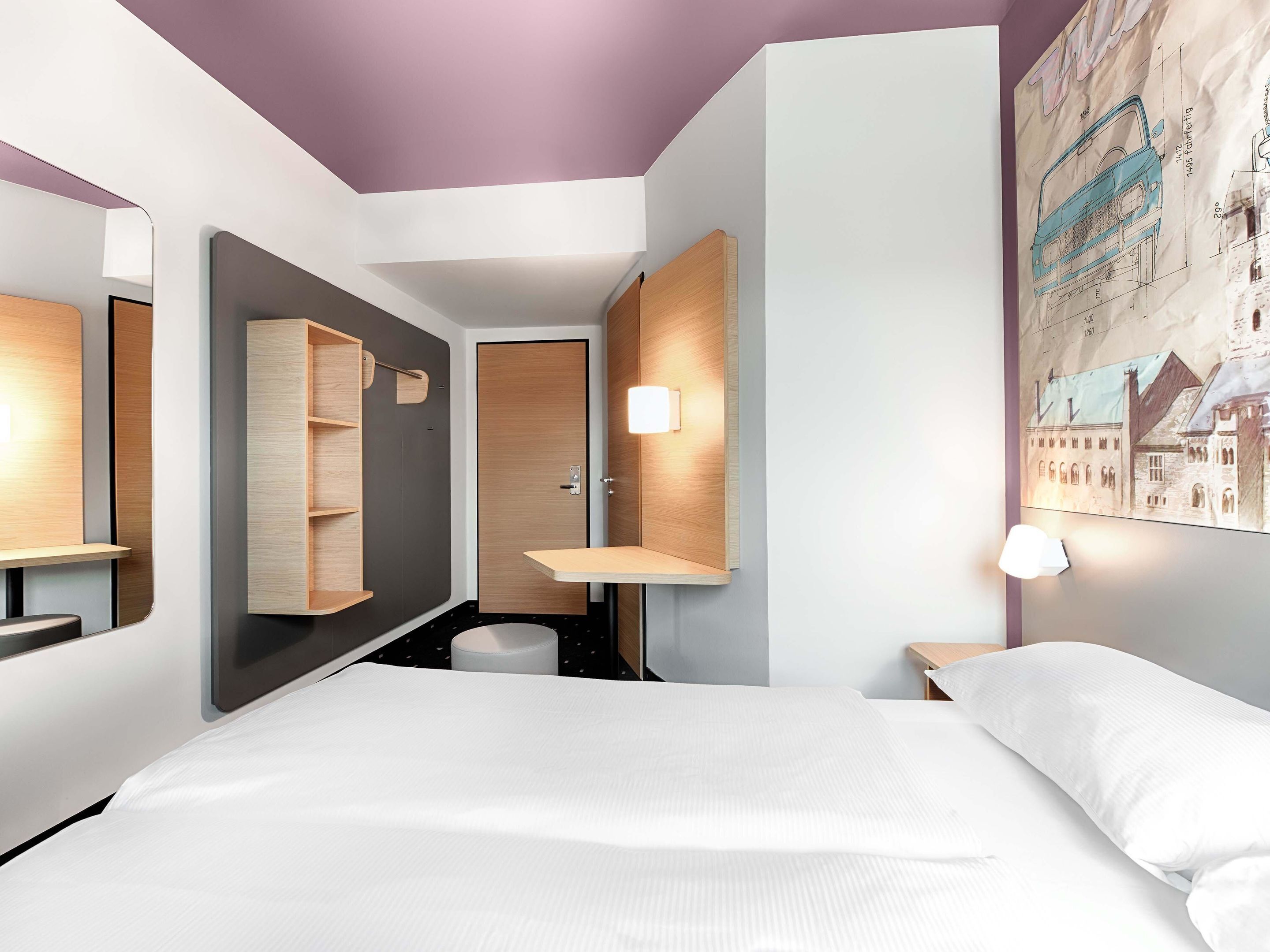 Ein modernes Hotelzimmer mit einem großen Bett, einem Holzschrank, einem Spiegel und einem an der Wand befestigten Regal.