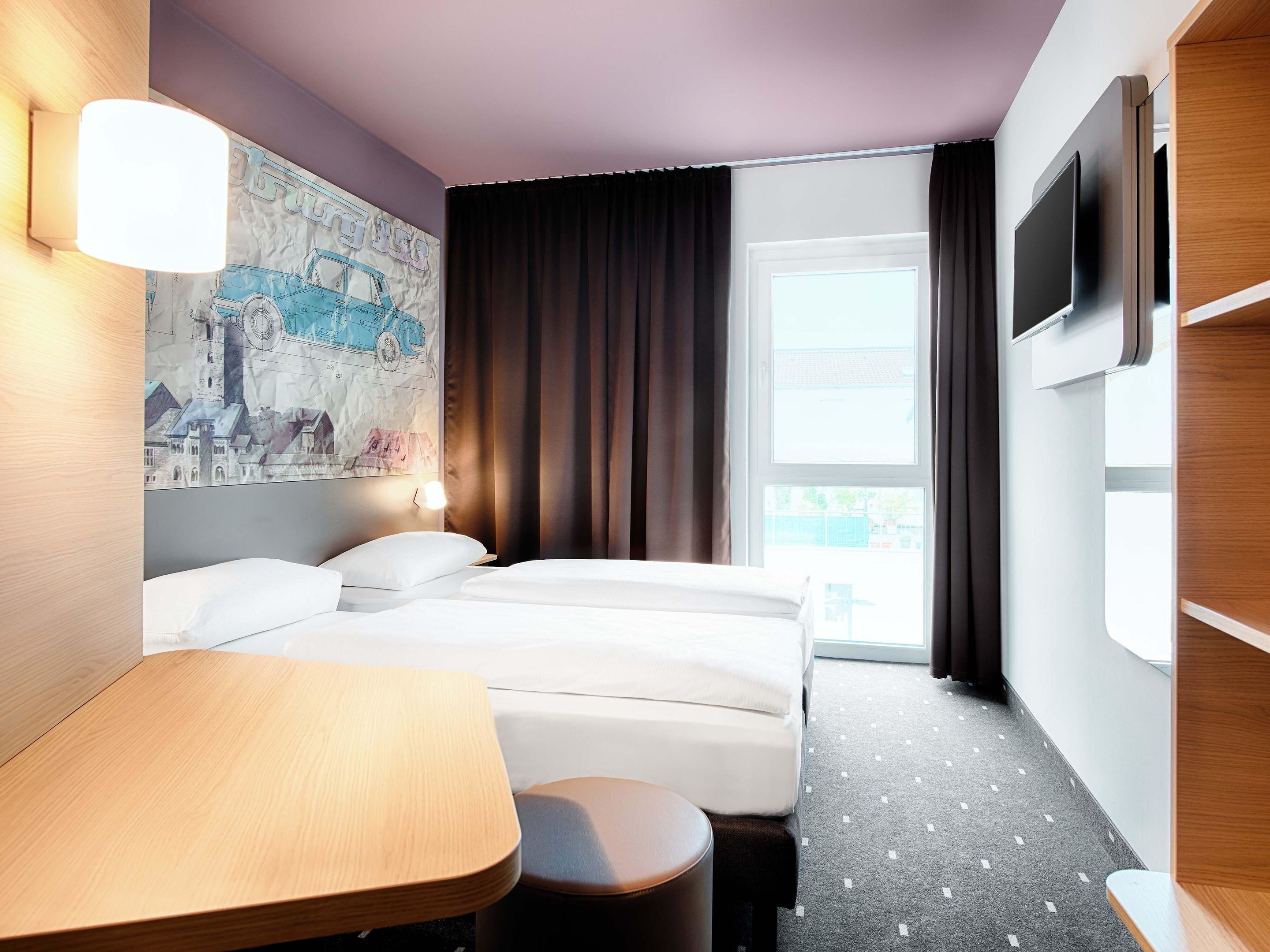 Ein Hotelzimmer mit Bett, Schreibtisch, einer Karte an der Wand und einem Fernseher.
