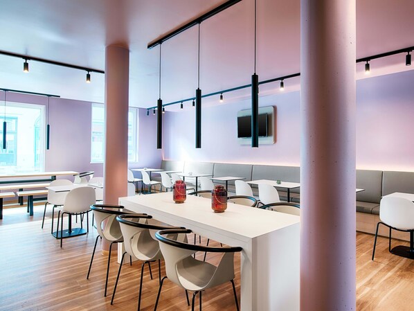 Een moderne eetruimte met witte tafels en stoelen, een lange balie en hanglampen.