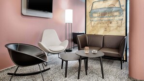 Un salon moderne doté d’un téléviseur à écran plat, d’une grande fresque murale représentant les plans d’un véhicule et de sièges contemporains.