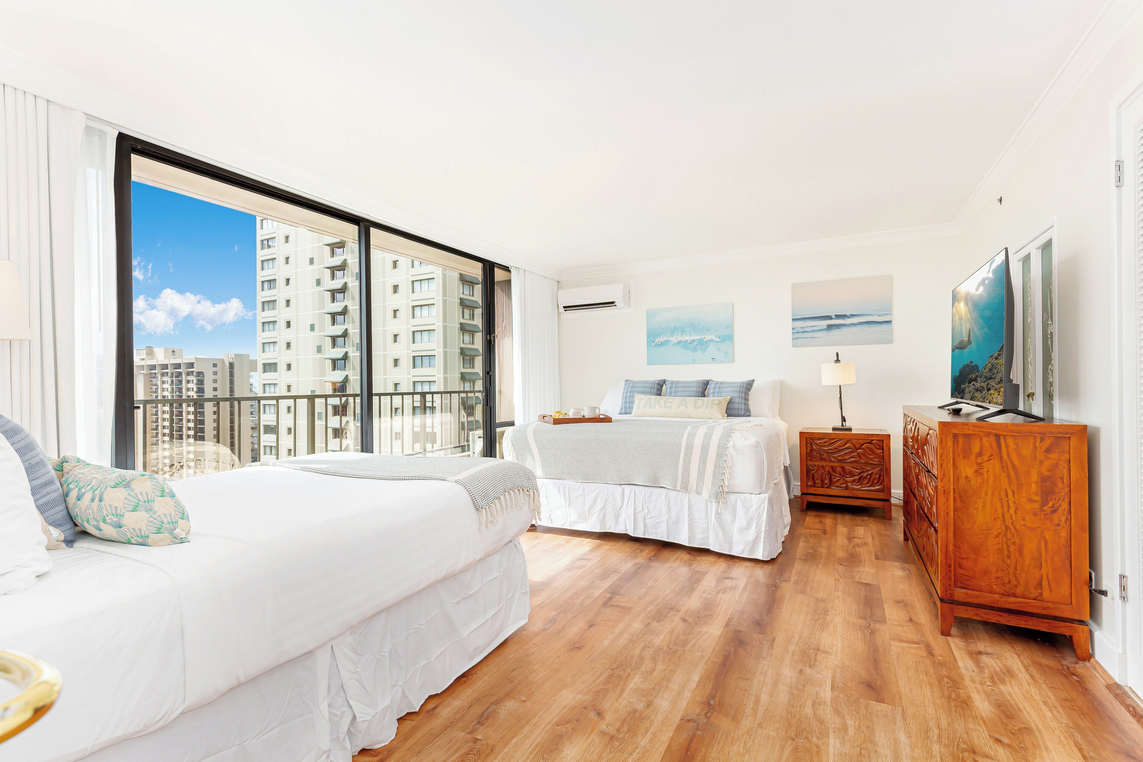 Ein modernes Schlafzimmer mit zwei Betten, einer Holzkommode und einem großen Fenster mit Blick auf die Stadt.