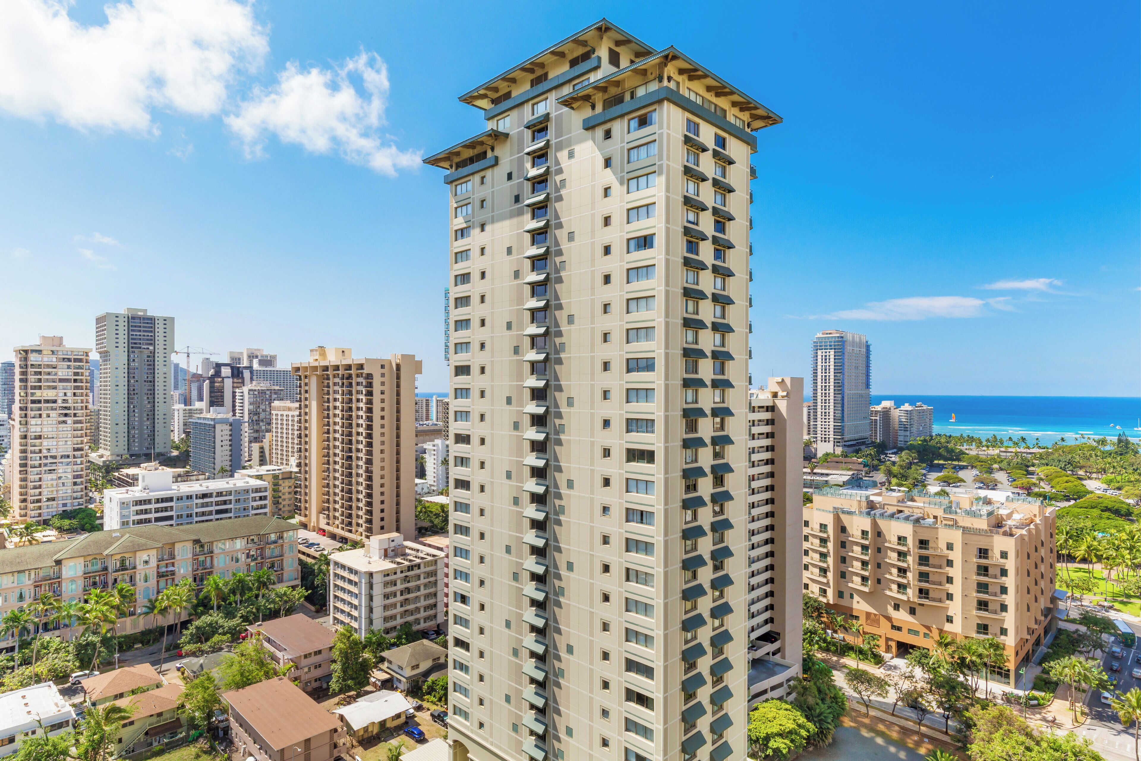 A high-rise building with multiple balconies, surrounded by other high-rise buildings and a coastal view.