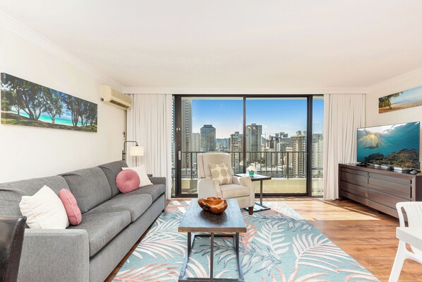 A modern living room with a grey sofa, a coffee table, and a city view through large windows.
