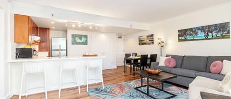 A modern living room with a grey sofa, white chairs, and a dining area with a table and chairs.