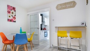 Una cocina moderna con armarios blancos, una campana extractora de acero inoxidable y un letrero en la pared que dice 'Be our guest'.