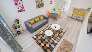 Una sala de estar moderna con un sofá gris, sillas coloridas, una mesa de centro y una zona de comedor con una mesa blanca y sillas amarillas.