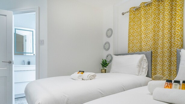 Habitación de hotel con dos camas, baño con espejo y cortina amarilla estampada.