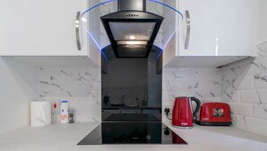 Una cocina moderna con una placa de inducción negra, una cafetera roja y una campana extractora de acero inoxidable.