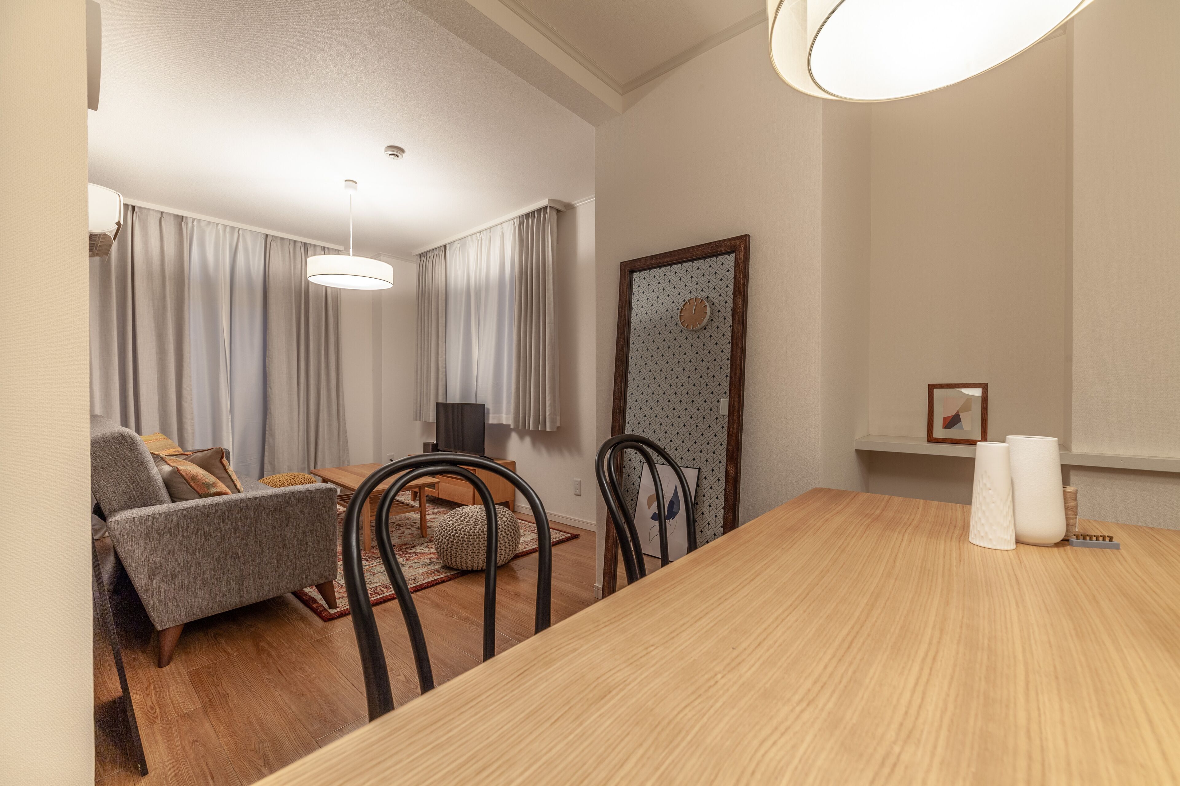 A modern living room with a dining table, chairs, a sofa, and a large window with curtains.